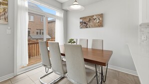 A dining area with a wooden table and four chairs, a pendant light, and a painting on the wall. - Cedar Nest - 5 Beds, 3.5 Baths, 2 Park, Backyard (Pickering)