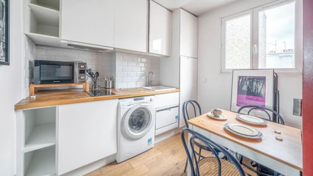 Una cocina compacta con armarios blancos, un microondas, una lavadora y un comedor con mesa y sillas.