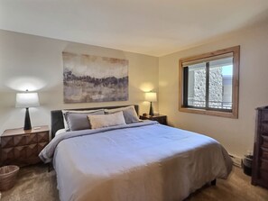 A bedroom with a bed, two bedside tables, a nightstand, a window with a view, and a painting on the wall. - Plaza 538 at Woodcreek — 100 Yds to Silver Queen | 2 Kings | Crested Butte (Crested Butte)