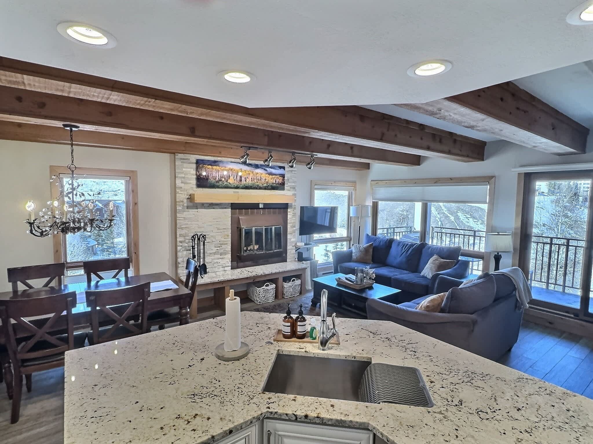 A spacious living area with a fireplace, a dining table, and a large window overlooking a snowy landscape.