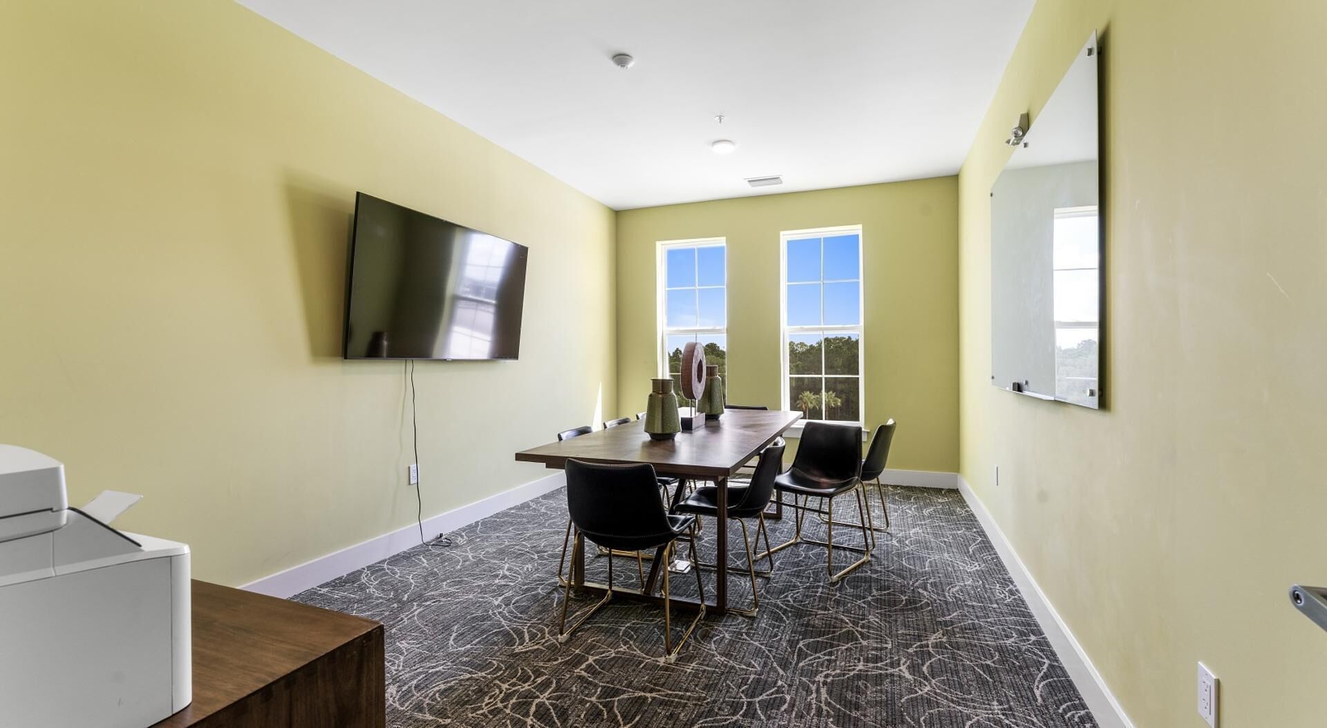 A conference room with a long table, four chairs, a flat-screen TV, and a whiteboard.