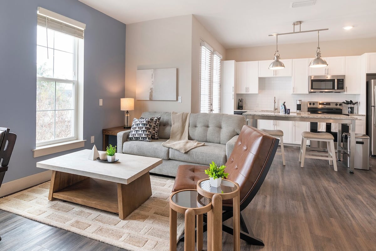 Una sala de estar moderna con un sofá gris, una mesa de centro de madera y un sillón de cuero.