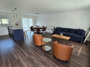 Eine moderne Küche mit Kochinsel, Essbereich mit rundem Tisch und Stühlen, ein blaues Sofa und zwei Ledersessel.