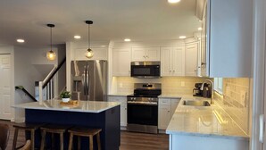 A modern kitchen with white cabinets, stainless steel appliances, a central island with stools, and a wooden floor. - Rumsey Island! (Joppatowne)