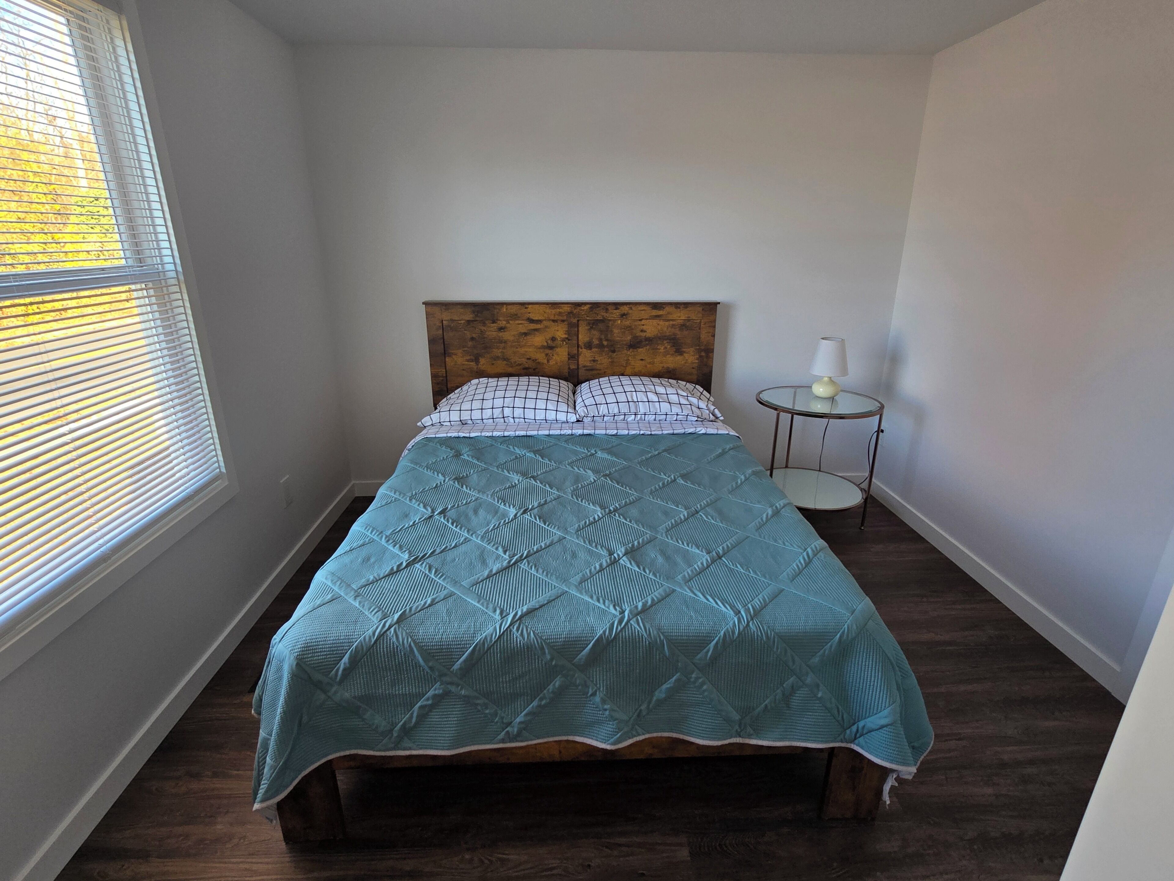 A bedroom with a bed, a bedside table with a lamp, and a window with blinds.