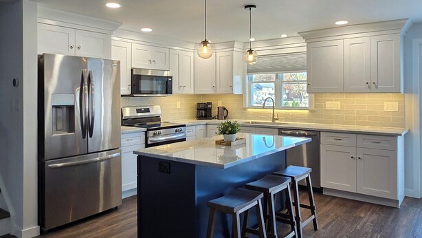 A modern kitchen with stainless steel appliances, a central island with bar stools, pendant lighting, and a view of the outdoors. - Rumsey Island! (Joppatowne)