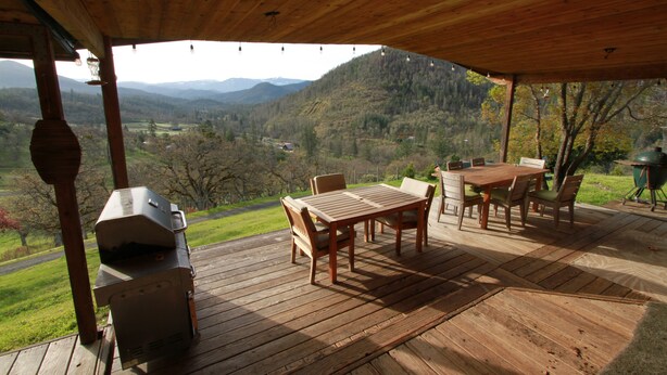 Eine Holzdar Terrasse mit Tisch und Stühlen, mit Blick auf ein Tal und Berge im Hintergrund.