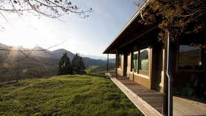 Ein modernes Haus mit einer Holterrasse mit Blick auf einen grasbewachsenen Hang und entfernte Berge.