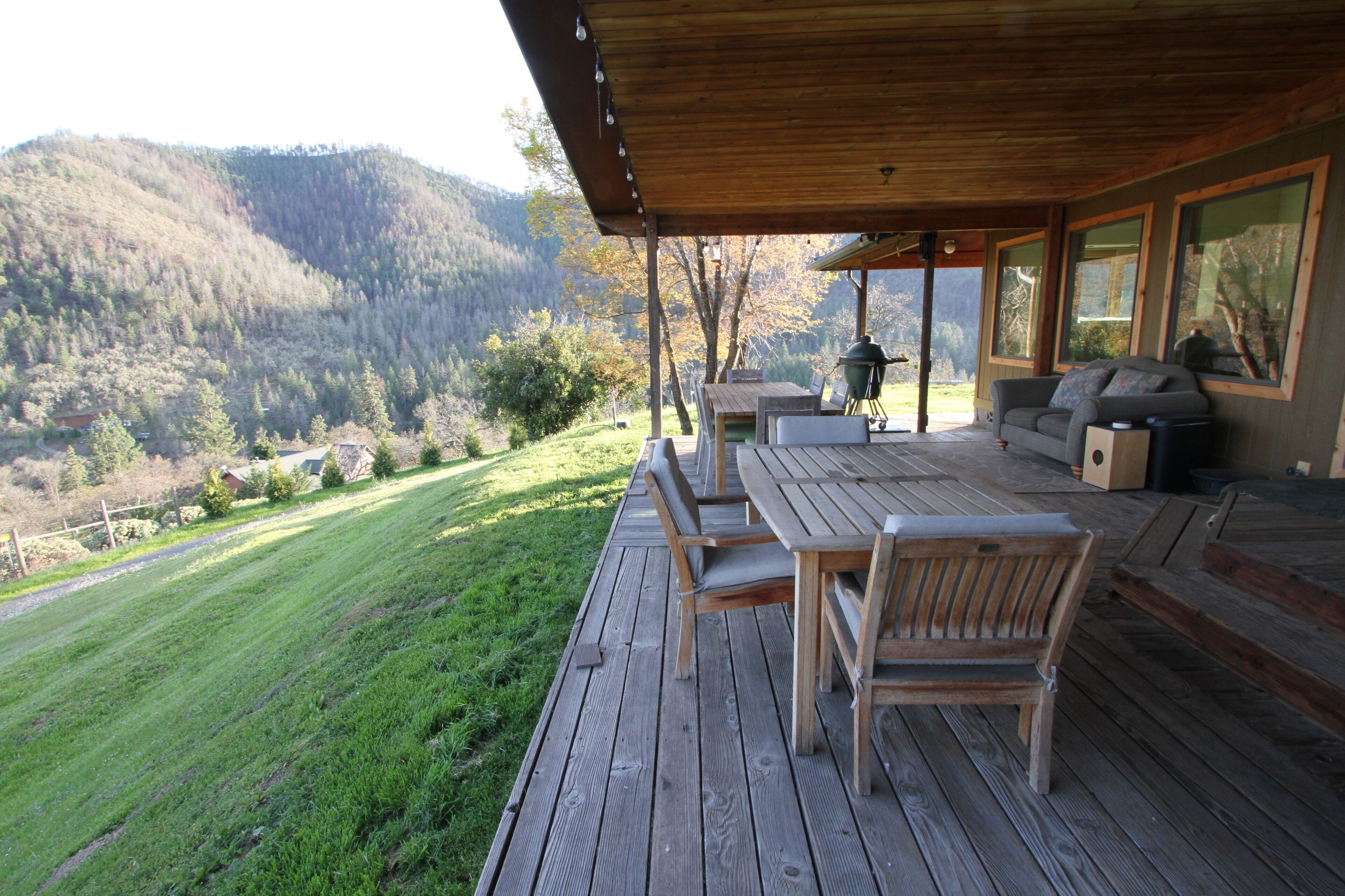 Um deck de madeira com mobiliário externo, com vista para uma paisagem montanhosa.