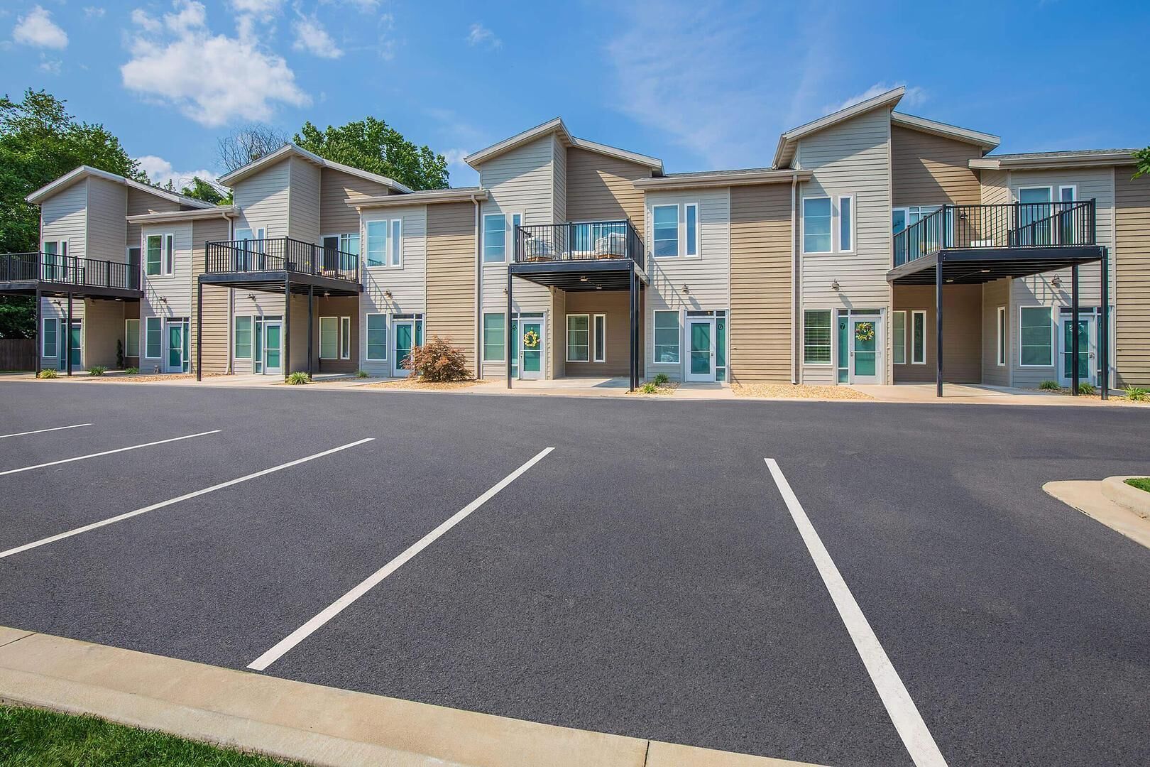 A row of modern apartment buildings with balconies, a parking lot, and a clear sky.