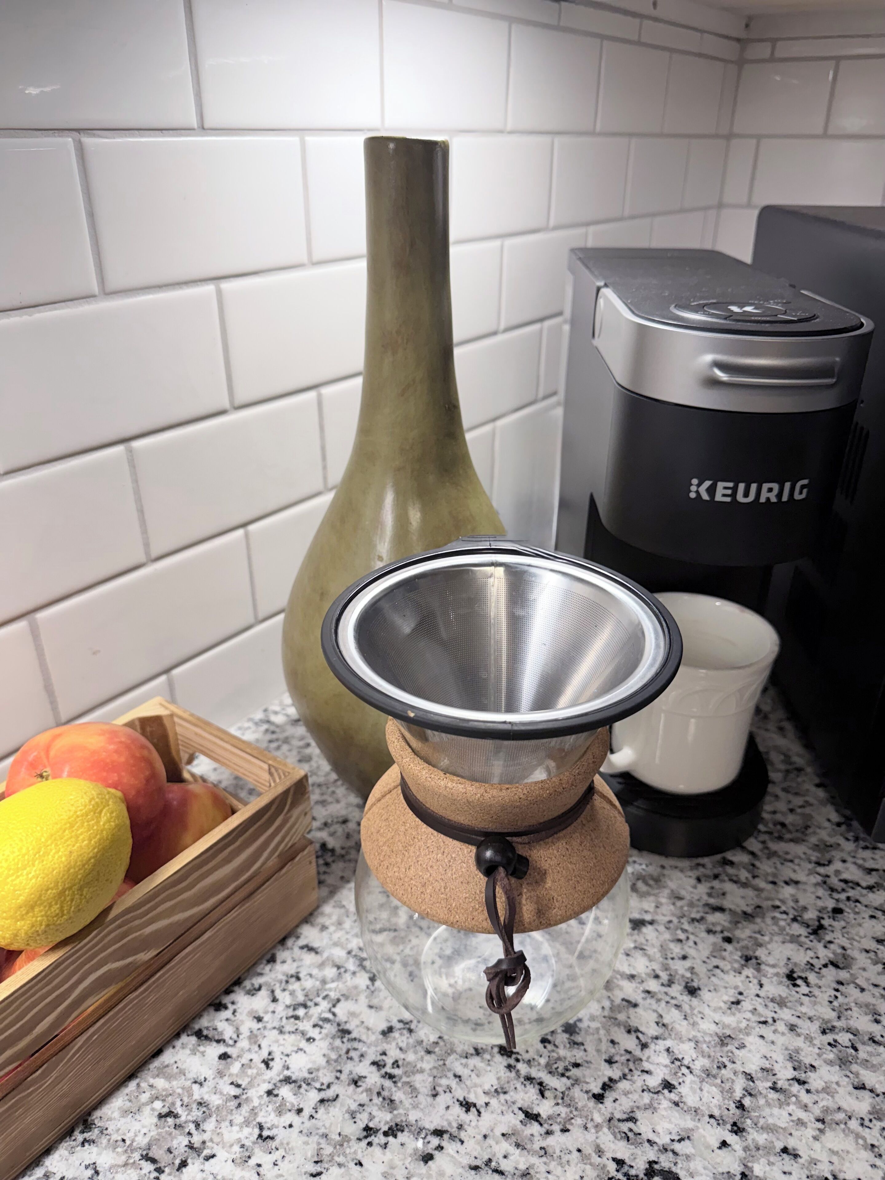 Un plan de travail de cuisine avec une machine à café, un panier de fruits et un moulin à café.