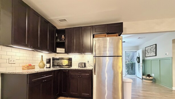 Una cocina moderna con armarios de madera oscura, un refrigerador de acero inoxidable, un microondas y una encimera de madera.