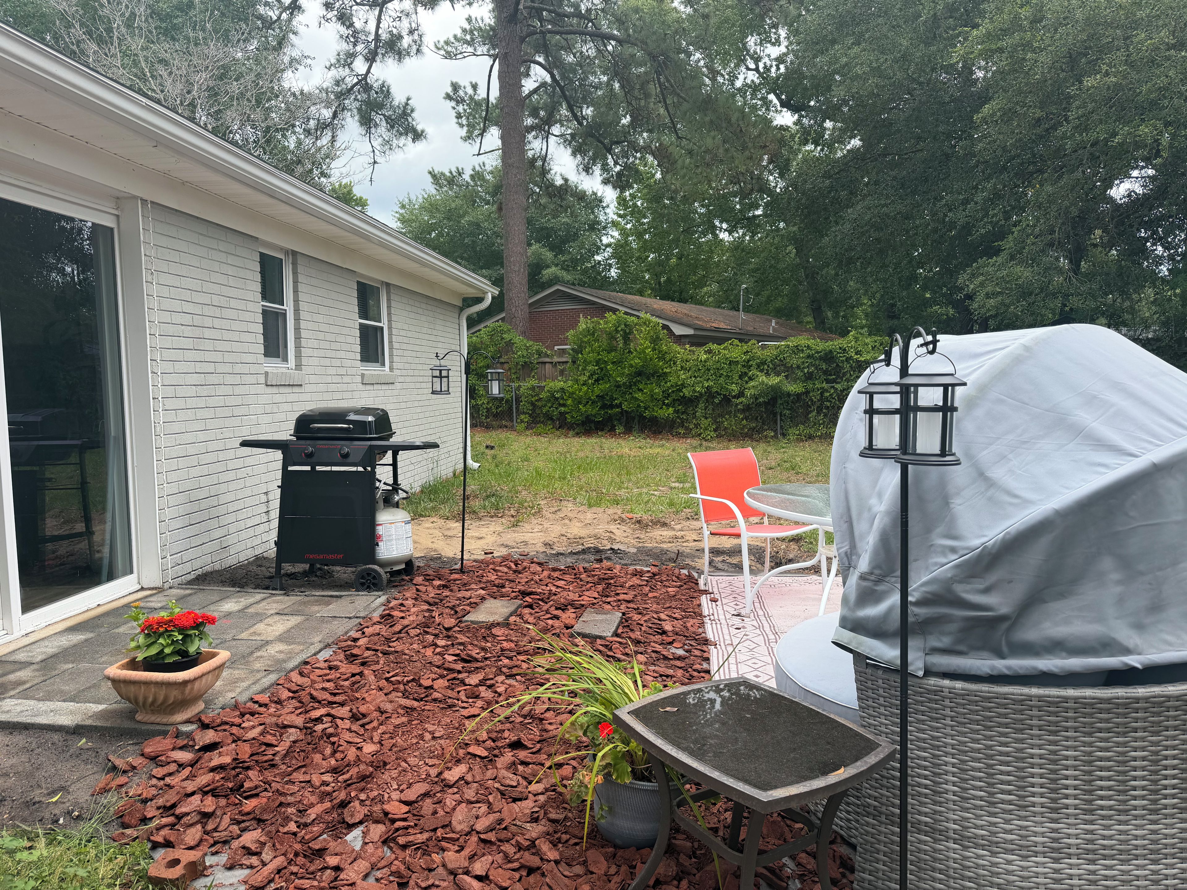 A backyard with a barbecue grill, outdoor furniture, and a covered table.