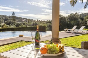 A table with a bottle of champagne, glasses, and a plate of fruit by a poolside with lounge chairs in the background. - Villa Nobleza, a private oasis with a pool and gym just a stone's throw from downtown! (Selva)