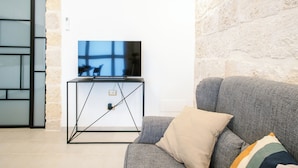 Ein Wohnzimmer mit grauem Sofa, schwarzem TV-Schrank und Steinwand.
