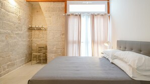 Ein Schlafzimmer mit Steinwand, einem Bett mit weißen Leinentüchern, einem Holz-Kopfende und einem Fenster mit Vorhängen.