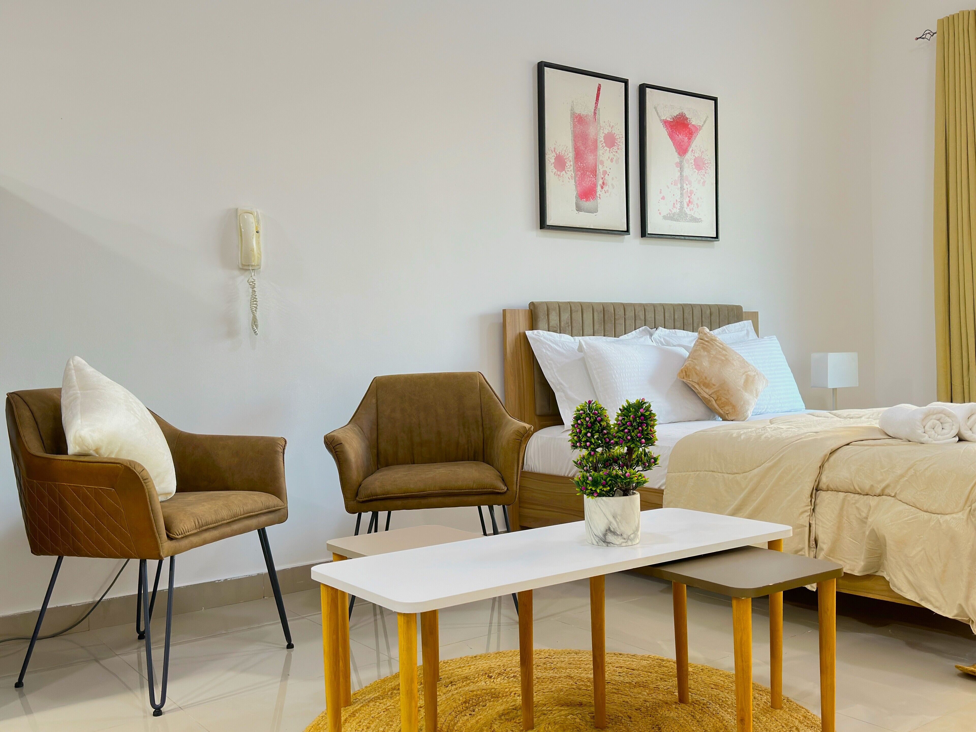 A hotel room with a bed, two chairs, a small table, and a wall-mounted light.