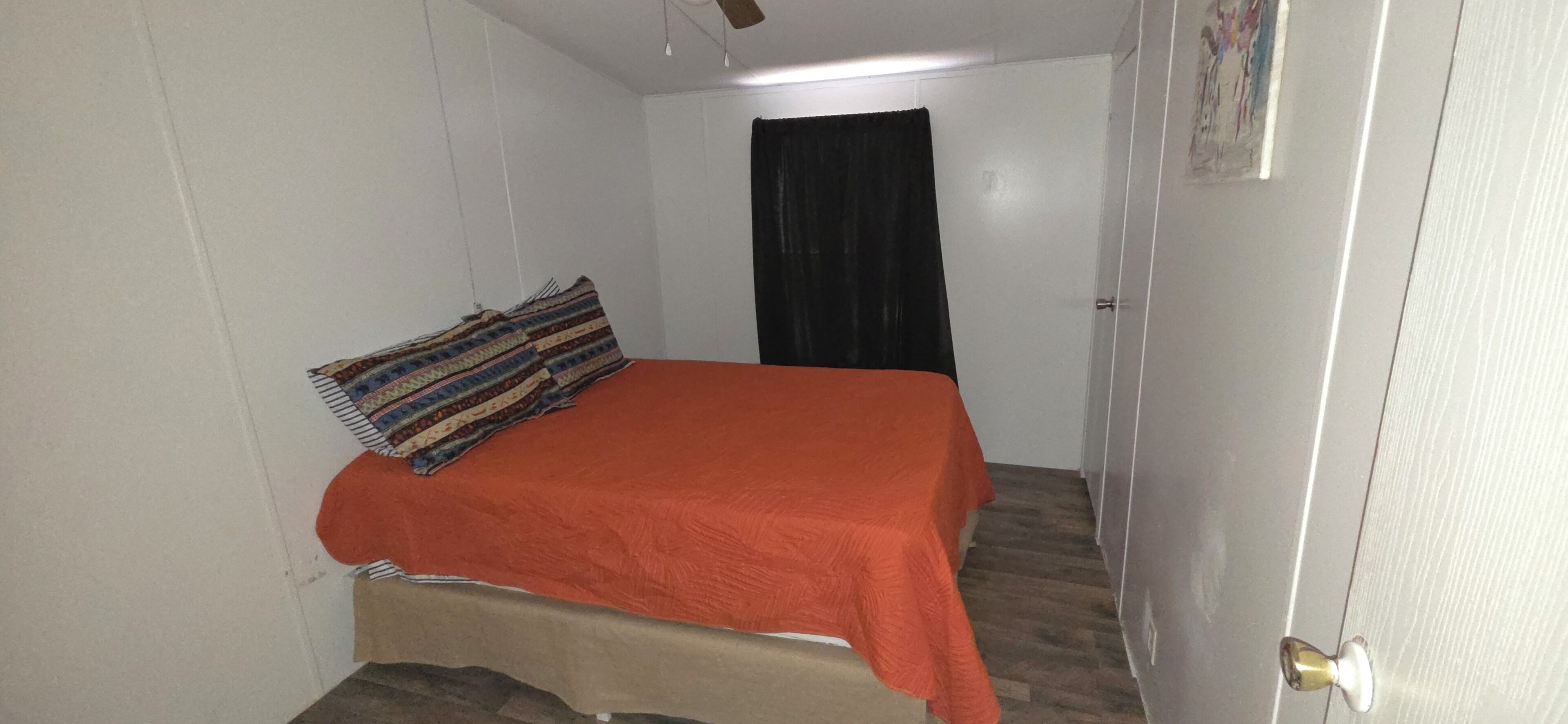 Een kleine kamer met een bed, een deur en een gordijn.