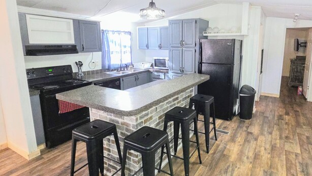 Una cocina con una isla central, taburetes de bar, un refrigerador y un microondas.