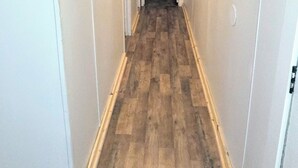 Un pasillo estrecho con suelo de madera y paredes blancas, que conduce a una puerta al final.