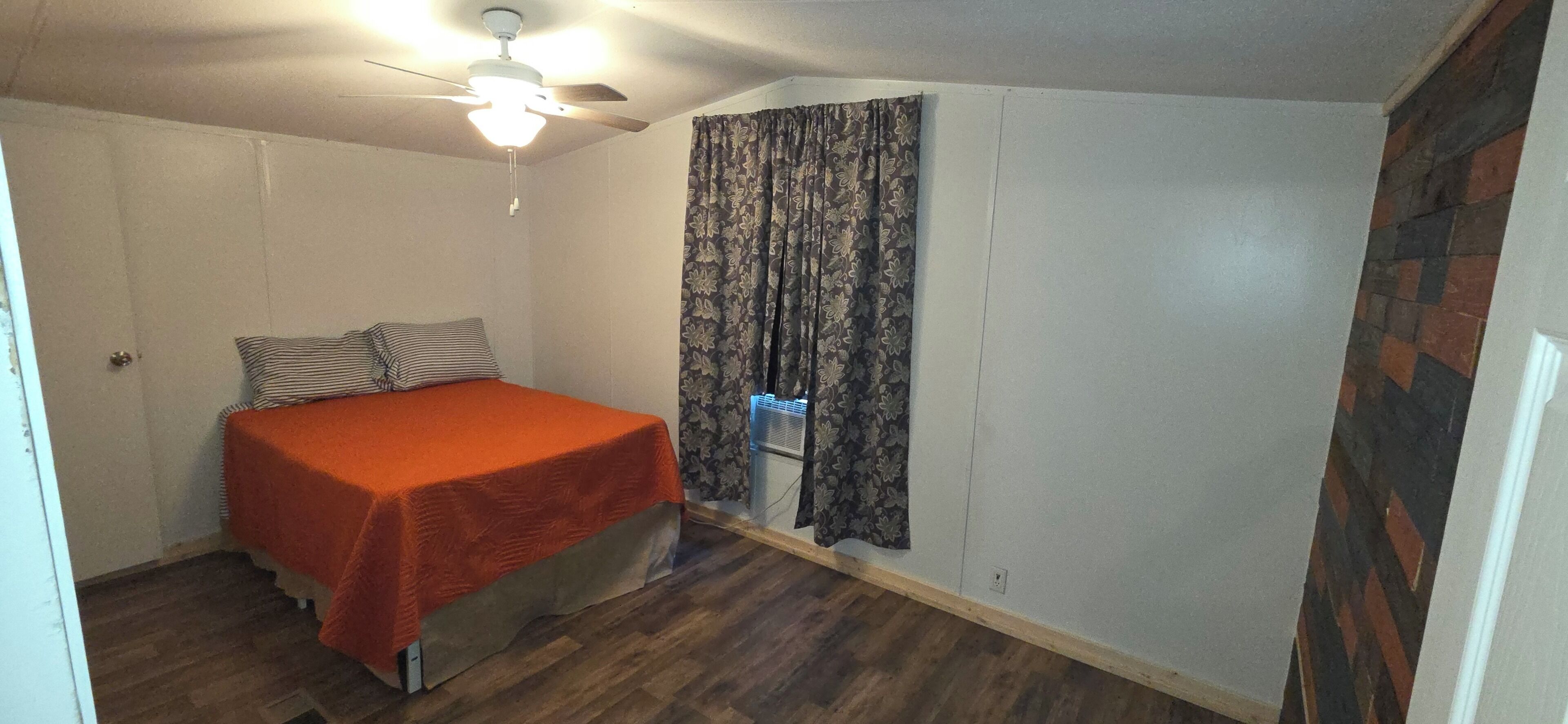 A bedroom with a bed, a ceiling fan, a window with curtains, and a radiator.