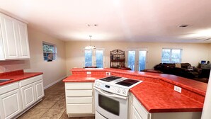 A kitchen with white cabinets, a red countertop, a built-in oven, and a double door window. - Grand Lagoon Retreat | Blue Angels & Boat Parking (Pensacola)