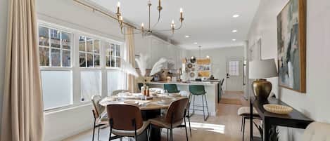 A dining area with a table set for four, a chandelier, and a view of the kitchen.