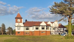 A building with a clock tower, multiple windows, and a grassy field in the foreground. - Sarah's Woodland Golf Stays (Waterloo)