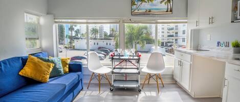 Un salón moderno con un sofá azul, sillas blancas, un televisor y vistas a la playa.