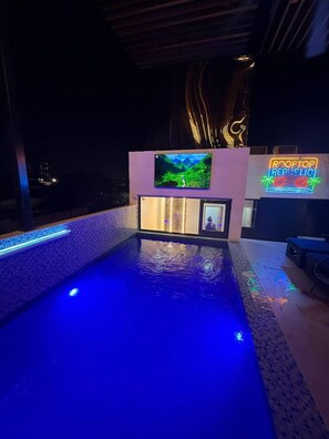 A swimming pool with blue lighting, a mounted TV screen, and a neon sign. - SkyGlow Suite | Luxury Queen + Rooftop Access (Cartagena de Indias)