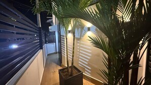 Un balcon orné d’un pot de fleurs, d’une applique murale et offrant une vue sur un bâtiment aux lignes horizontales.