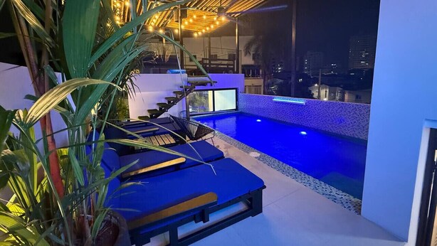 Une piscine sur le toit, agrémentée d’un éclairage bleu, de chaises longues et offrant une vue sur la ville la nuit.