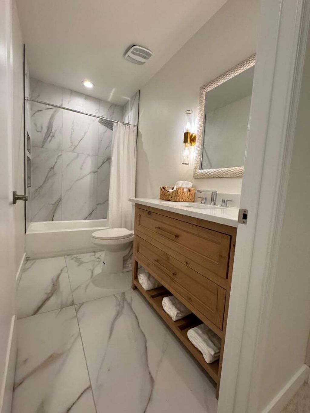 Et badeværelse med marmorgulv, badekar, toilet, trævaskemøbel med spejl og et håndklædestativ.