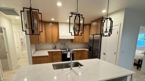 A modern kitchen with a large island, wooden cabinets, and pendant lighting. - Entire Home/Gated/King On suite (Tucson)
