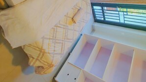 A bed with white bedding and a patterned pillow, a window with blinds, and a white bedside table with drawers. - ORVENA RESIDENCE (Kigali)