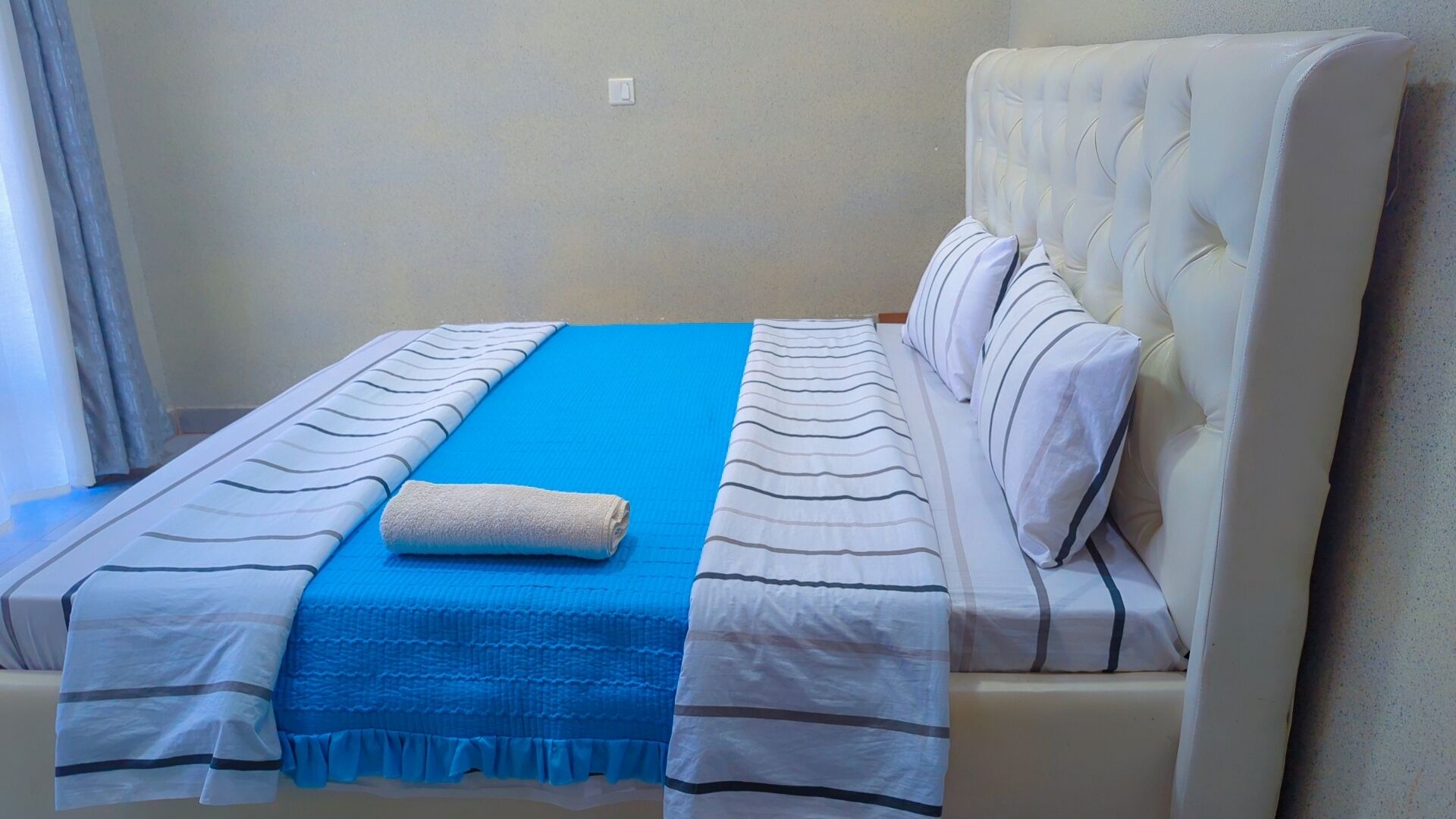 A neatly made bed with a blue blanket, white pillows, and striped bedspreads.