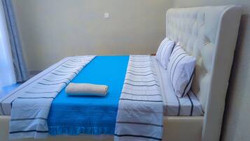 A neatly made bed with a blue blanket, white pillows, and striped bedspreads.