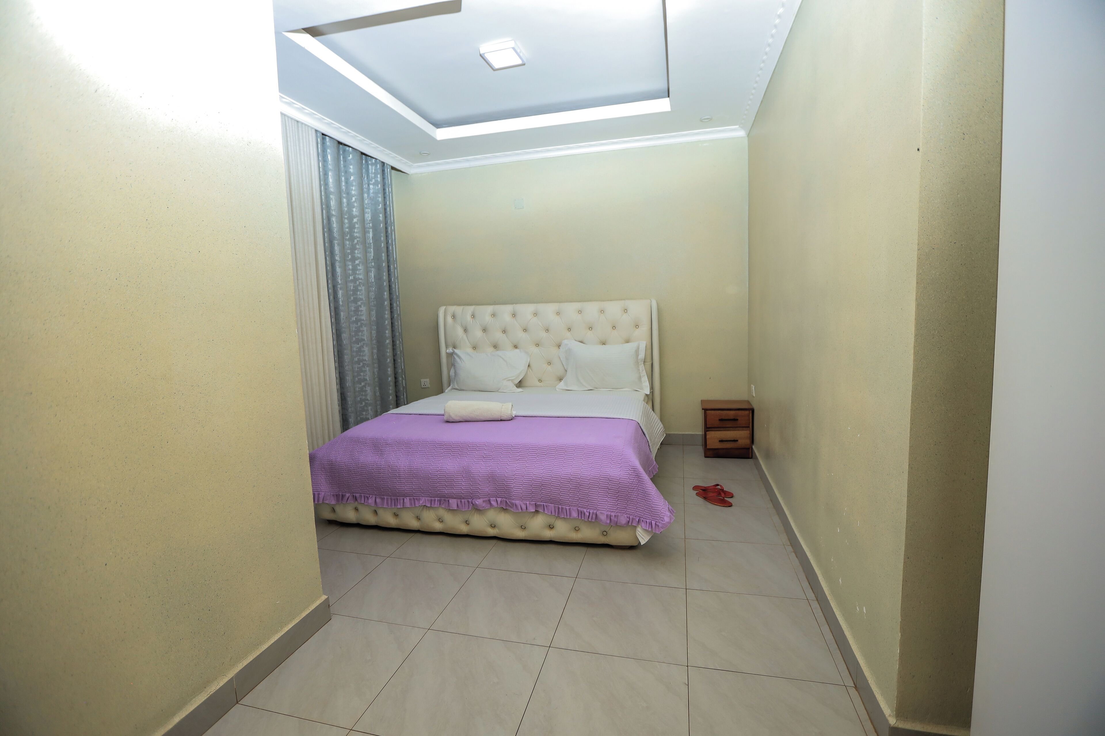 Un dormitorio con cama, luz de techo y mesita de noche.