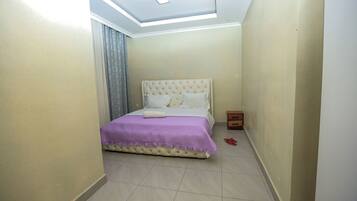 Un dormitorio con cama, luz de techo y mesita de noche.