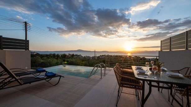 Una terraza en la azotea con piscina, zona de comedor y vistas a la puesta de sol sobre el mar.