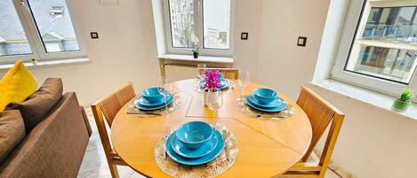 Un comedor con una mesa de madera redonda dispuesta para cuatro personas, rodeada de sillas de madera.