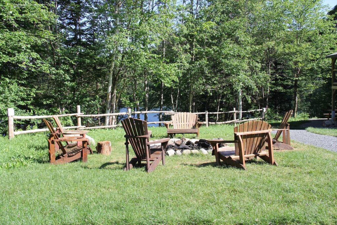 A wooden deck with Adirondack chairs and a fire pit surrounded by a wooden fence and trees.