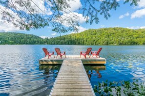 A wooden dock extending into a lake with four red Adirondack chairs on the dock.