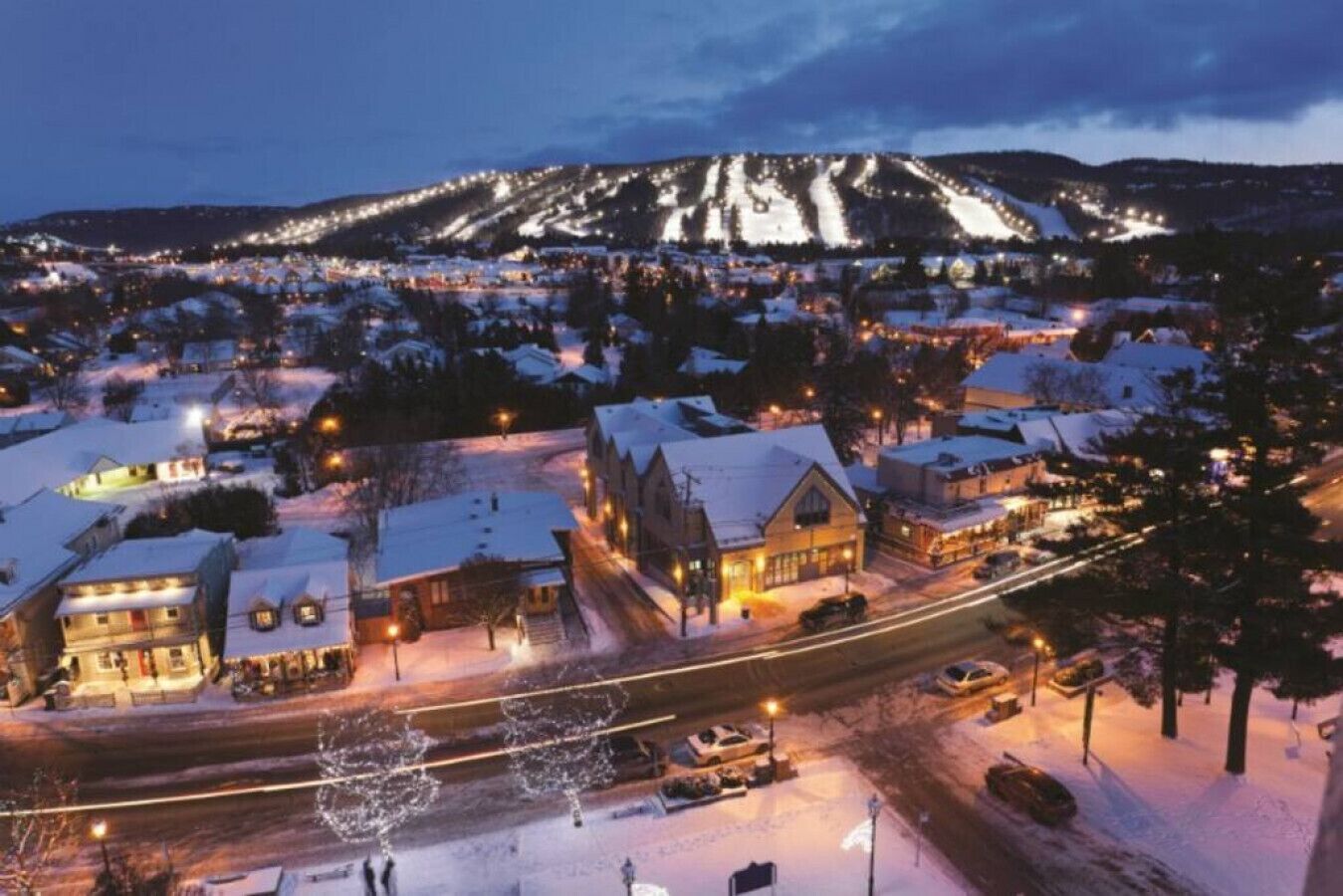 A snow-covered town at night with illuminated buildings and a mountain in the background.