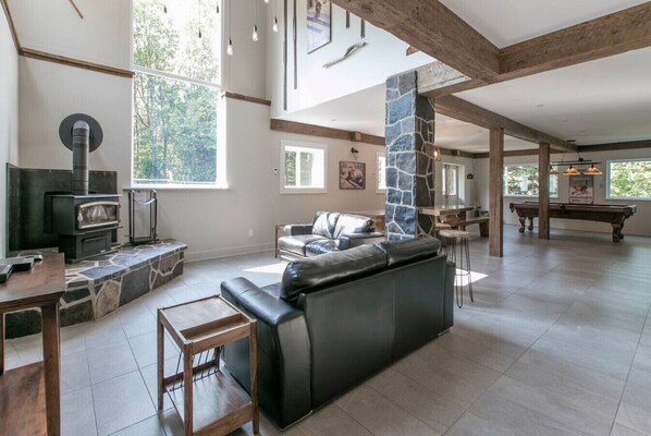 A spacious living area with a stone fireplace, leather sofa, and a pool table. - Grand chalet bord de lac (Saint-Adolphe-d`Howard)