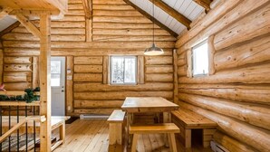 A log cabin interior with a wooden dining table, benches, a hanging light fixture, and a window. - Avec accès au Petit lac Long (Saint-Adolphe-d`Howard)