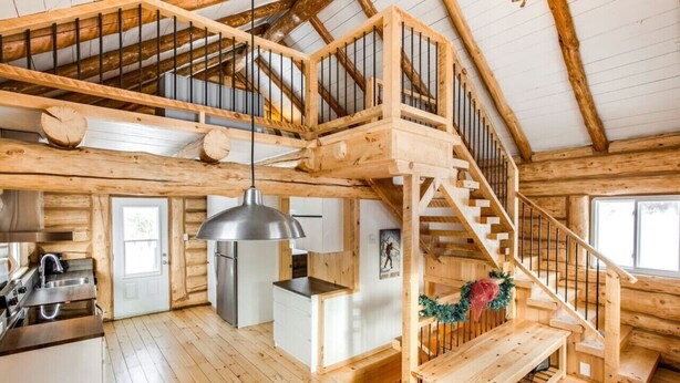 A spacious cabin with a high ceiling, wooden beams, a central staircase, a kitchen area, and a cozy seating area. - Avec accès au Petit lac Long (Saint-Adolphe-d`Howard)