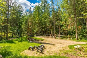 Un área boscosa con un sendero de tierra, una cerca de madera y columpios de neumático.