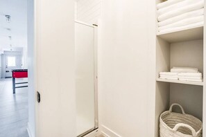 Habitación de hotel con una puerta blanca, un miniibar rojo y una repisa con toallas dobladas y una cesta tejida.