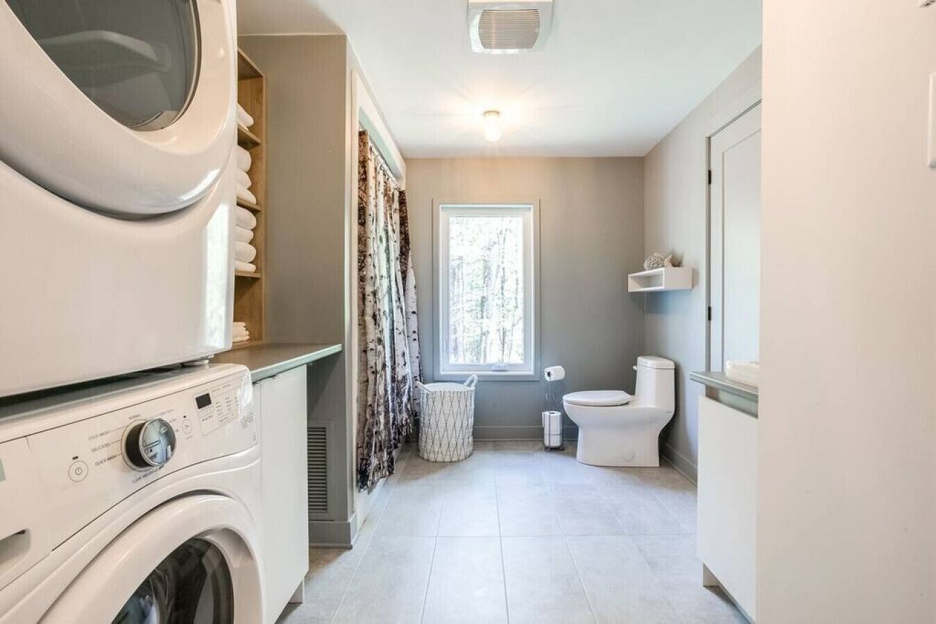 A laundry room with a washing machine, dryer, and a window with curtains.